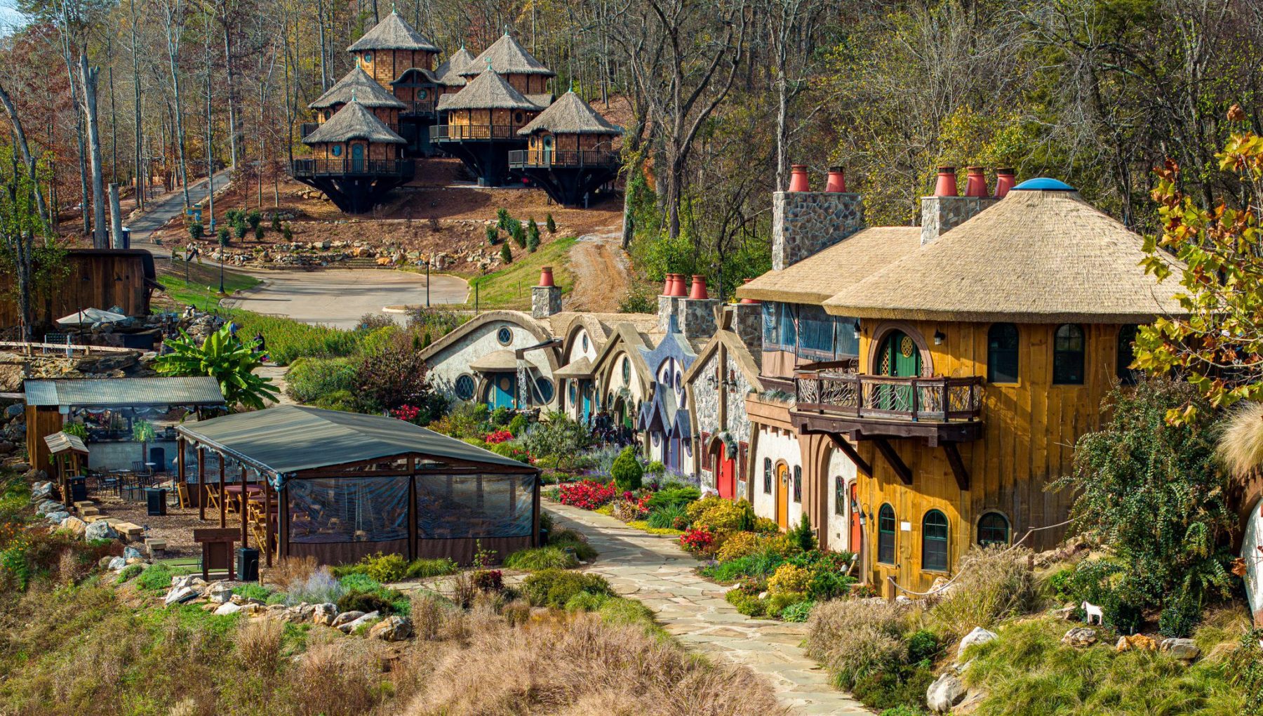Treehouses at Ancient Lore Village Fairytale village with whimsical houses, lush gardens, and forest backdrop under a clear sky.